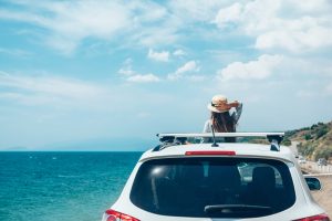 Imagen de espaldas de una chica sobre el toldo de un automóvil disfrutando del bleisure frente al mar