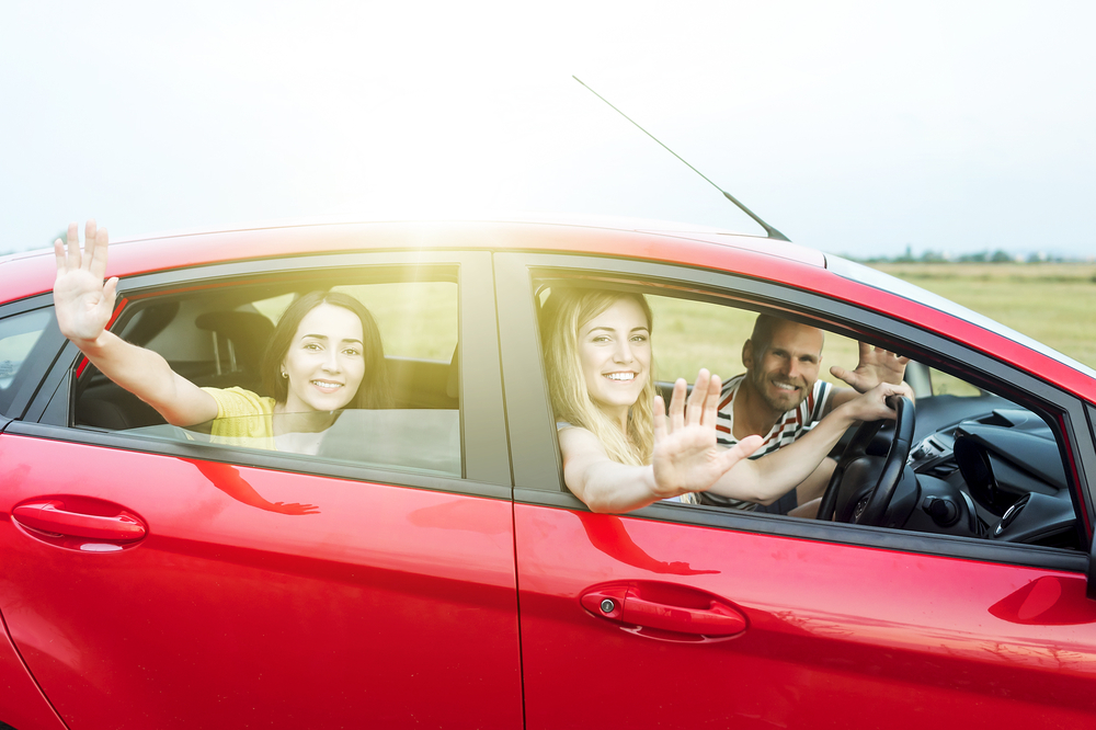 Familia de viaje sonrientes en automóvil rojo