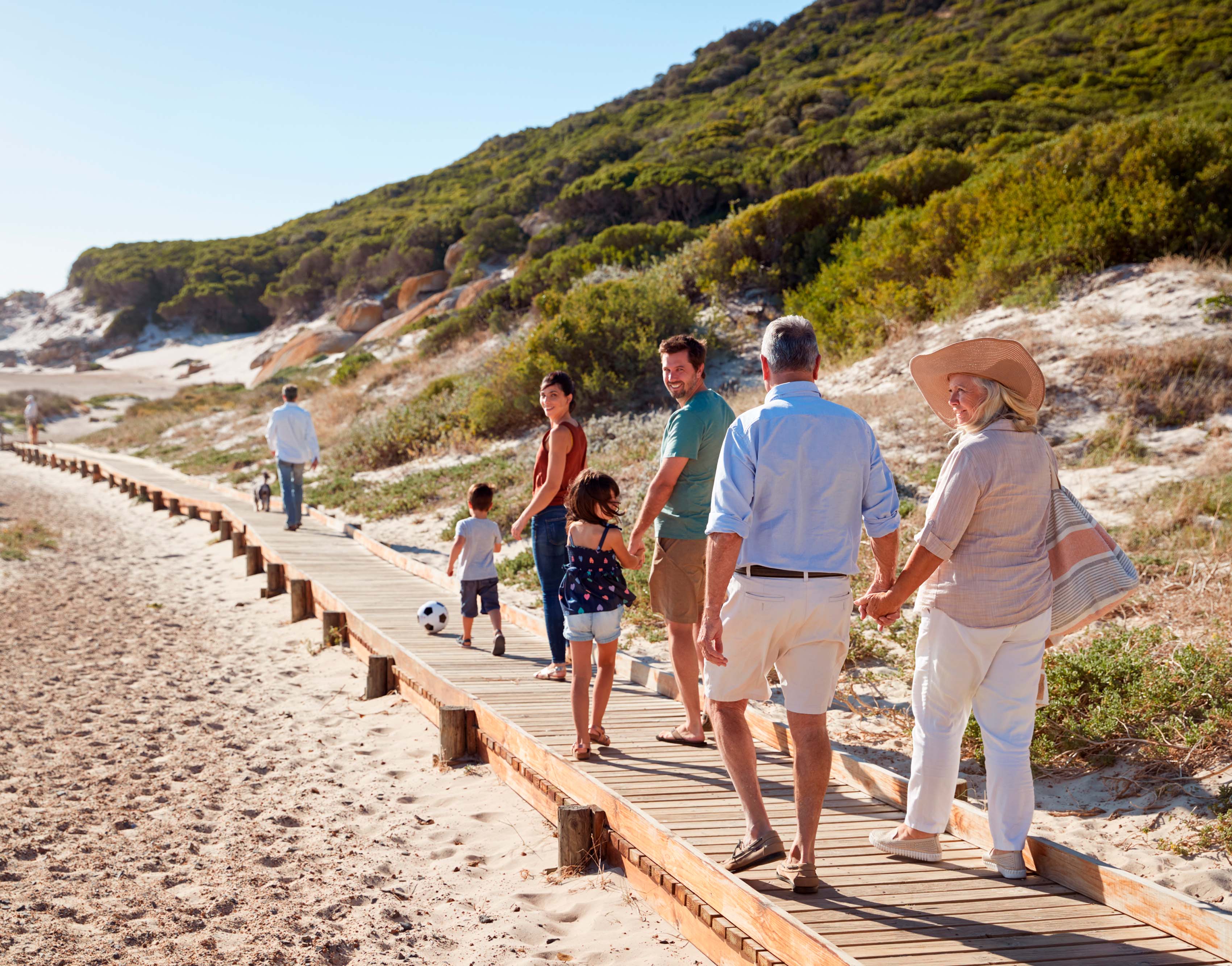 Abuelos y familia en playa vista de espaldas caminando sobre un puente de madera