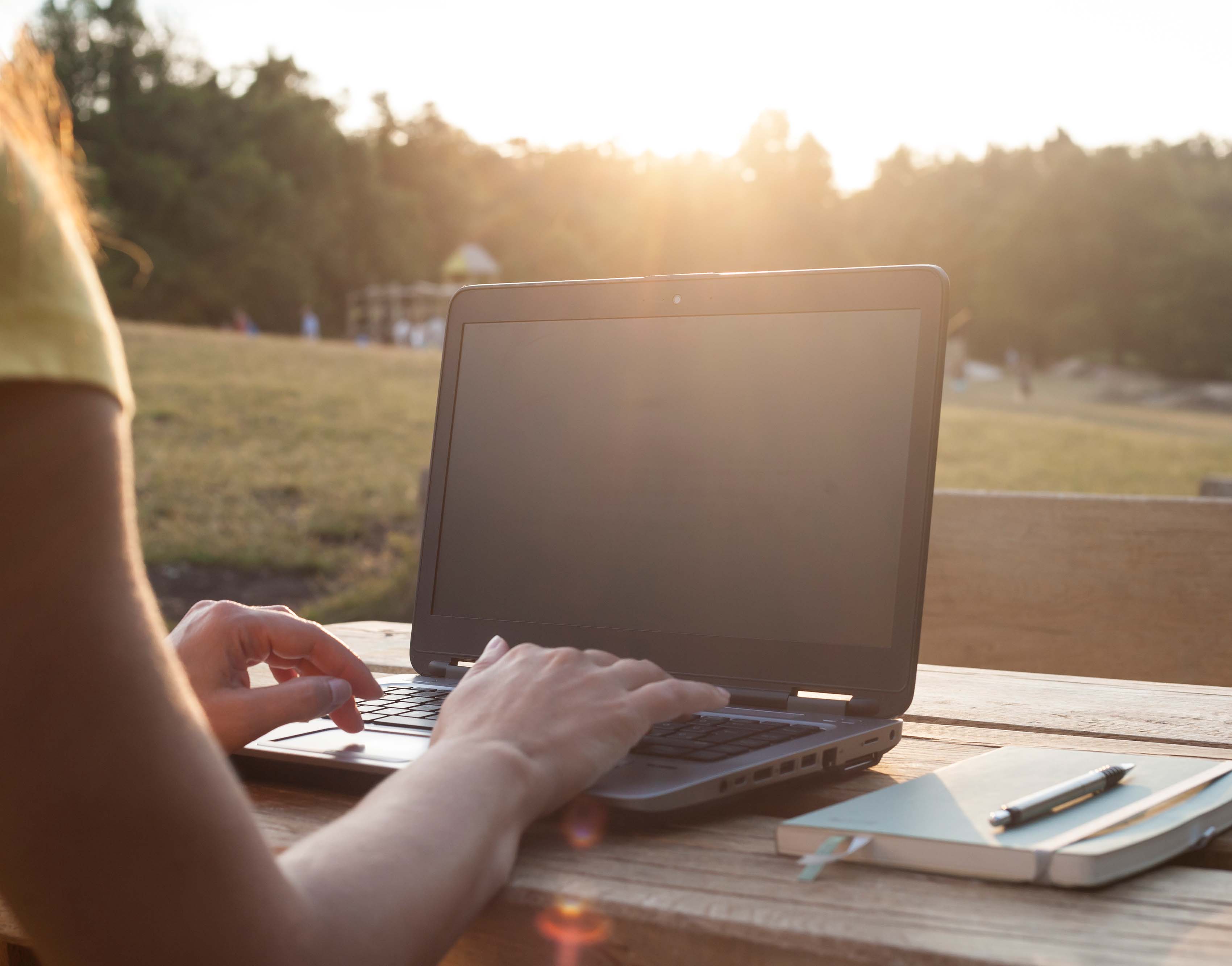 Imagen de unas manos de mujer trabajando en una laptop admirando un paisaje boscoso.