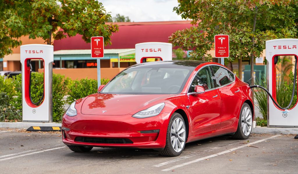Imagen del auto eléctrico Tesla Model 3 color rojo en una estación de carga Tesla