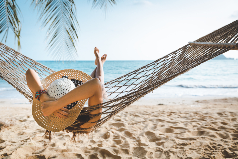Mujer en hamaca frente a la playa disfrutando sus vacaciones