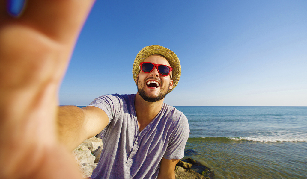 Feliz hombre de vacaciones riéndose de la playa tomando selfie, Tips para lograr fotos increíbles en cada uno de tus viajes 