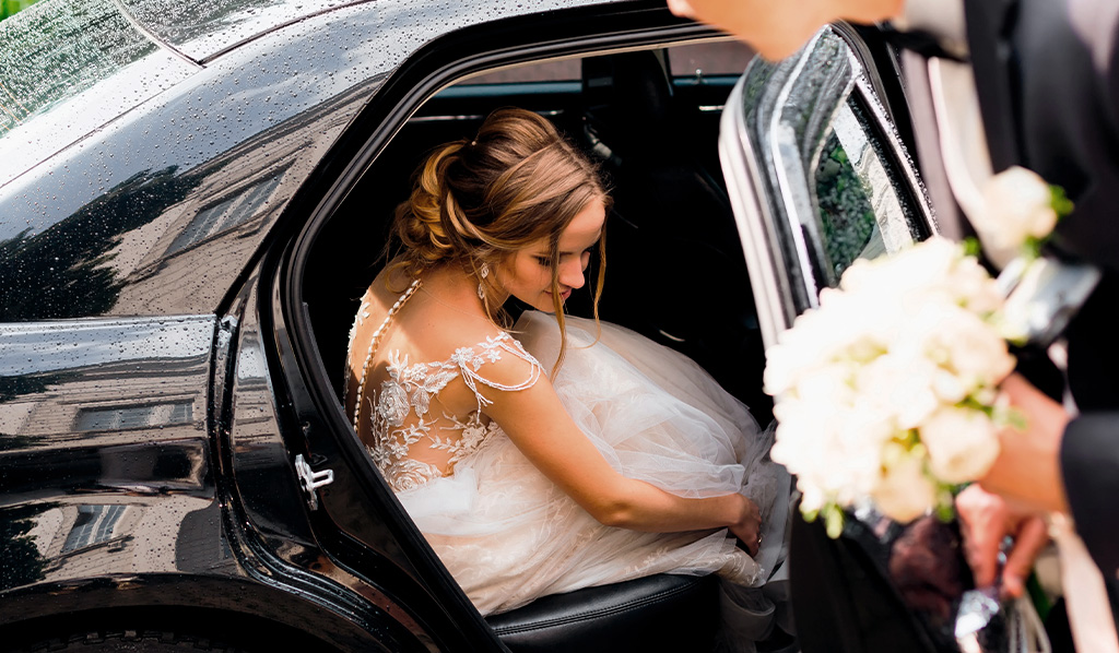 Novia se sienta en un auto negro y el novio quiere cerrar la puerta después