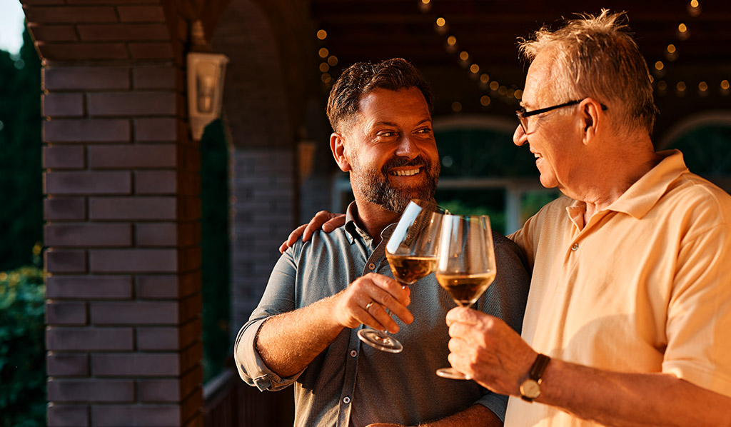 Feliz anciano y su hijo tostando con vino durante la familia se reúnen en una terraza.