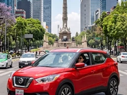 Un SUV Nissan Kicks de color rojo brillante de Avis México recorre la Zona Rosa de Ciudad de México junto al Ángel de la Independencia.