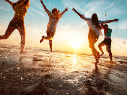Imagen a contraluz de un atardecer en la playa y unos amigos saltando muy felices