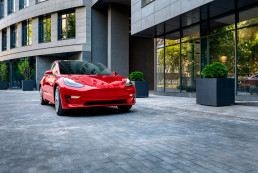 Automóvil Tesla rojo estacionandose en un espacio amplio citadino