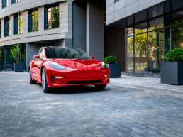 Automóvil Tesla rojo estacionandose en un espacio amplio citadino