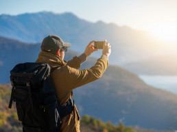 Viajero con una mochila y un smartphone parados en una montaña viajar solo: tips y motivos para hacerlo.