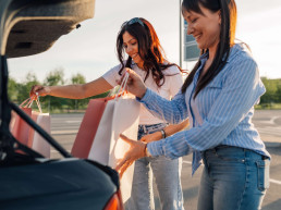 Jóvenes mujeres colocando sus bolsas de compras en el maletero del auto rentado