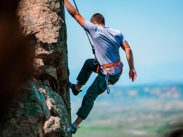 Un escalador de rocas encontrando un punto de apoyo en la empinada montaña que está escalando