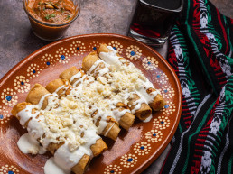 Tacos de patata frita con crema y queso en un plato de barro mexicano. Tacos dorados, comida mexicana.