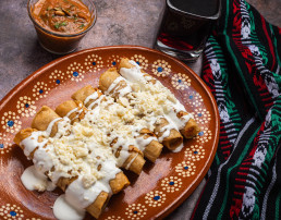 Tacos de patata frita con crema y queso en un plato de barro mexicano. Tacos dorados, comida mexicana.